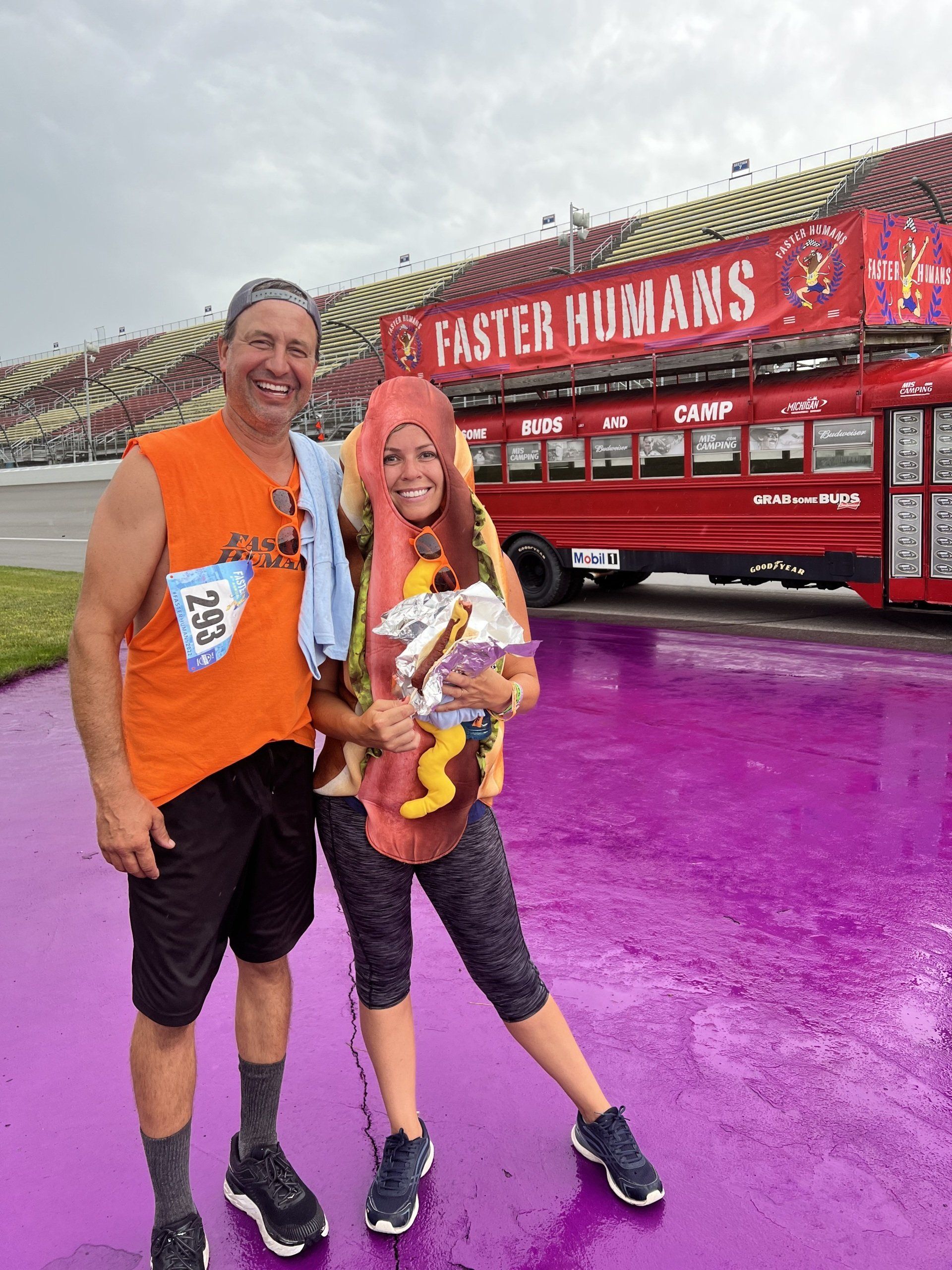A man and a woman are posing for a picture in front of a bus that says faster humans.