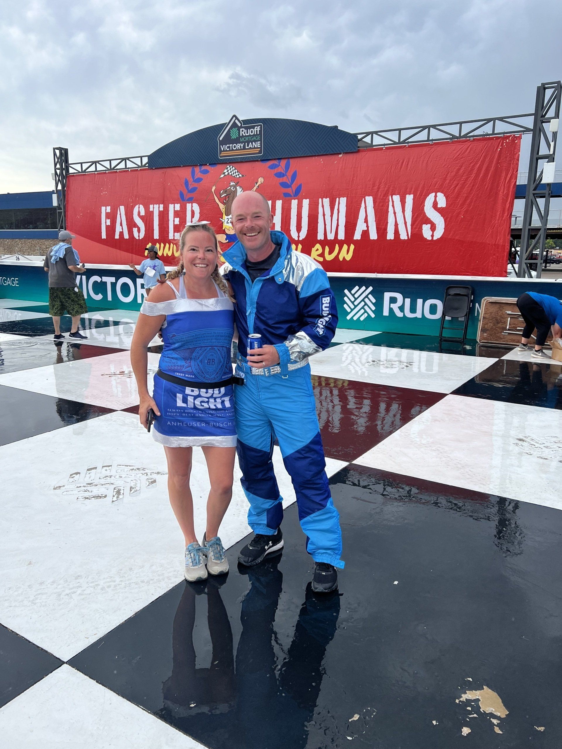 A man and a woman are posing for a picture in front of a sign that says faster humans.