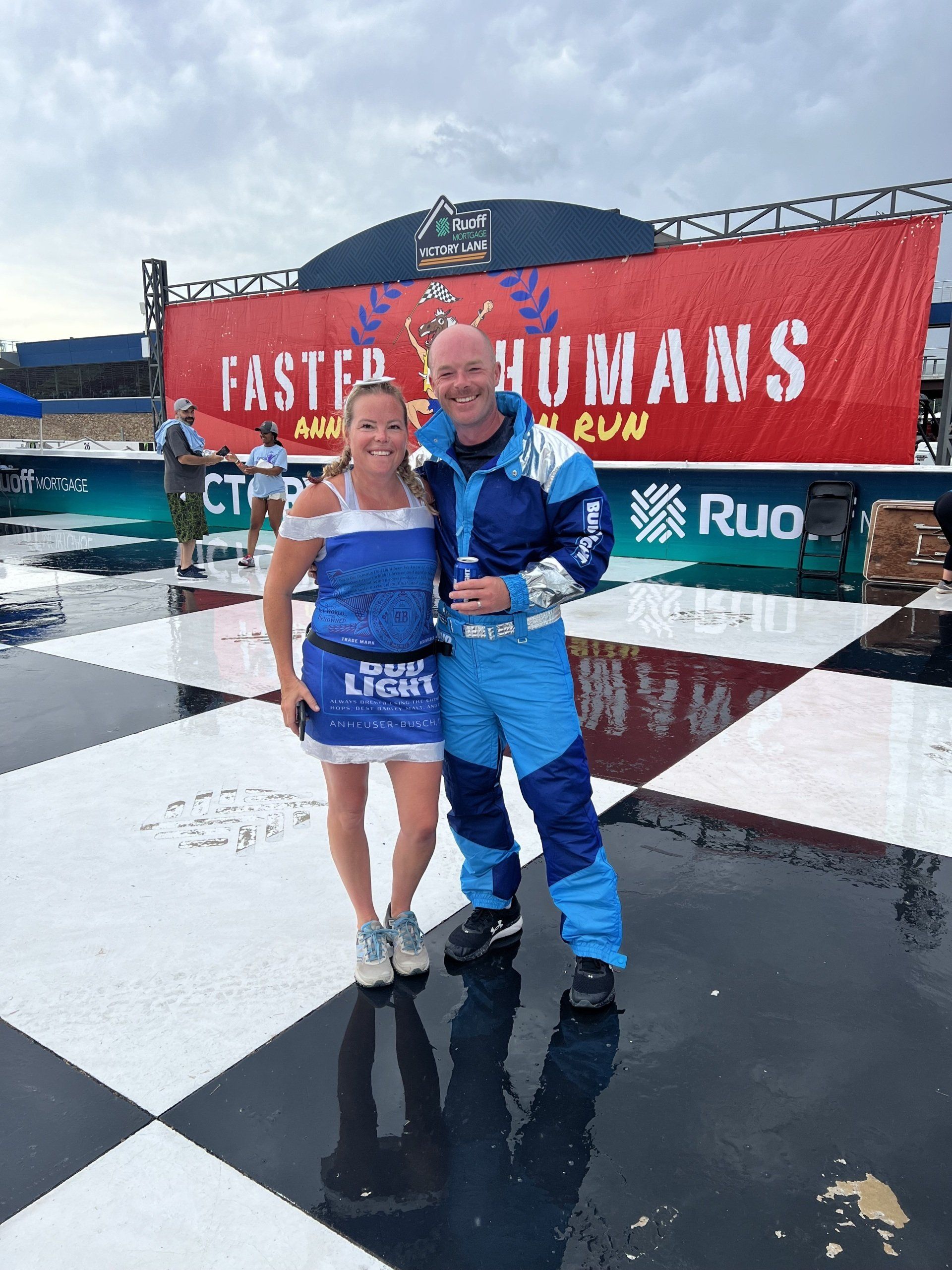 A man and a woman are posing for a picture in front of a sign that says faster humans.