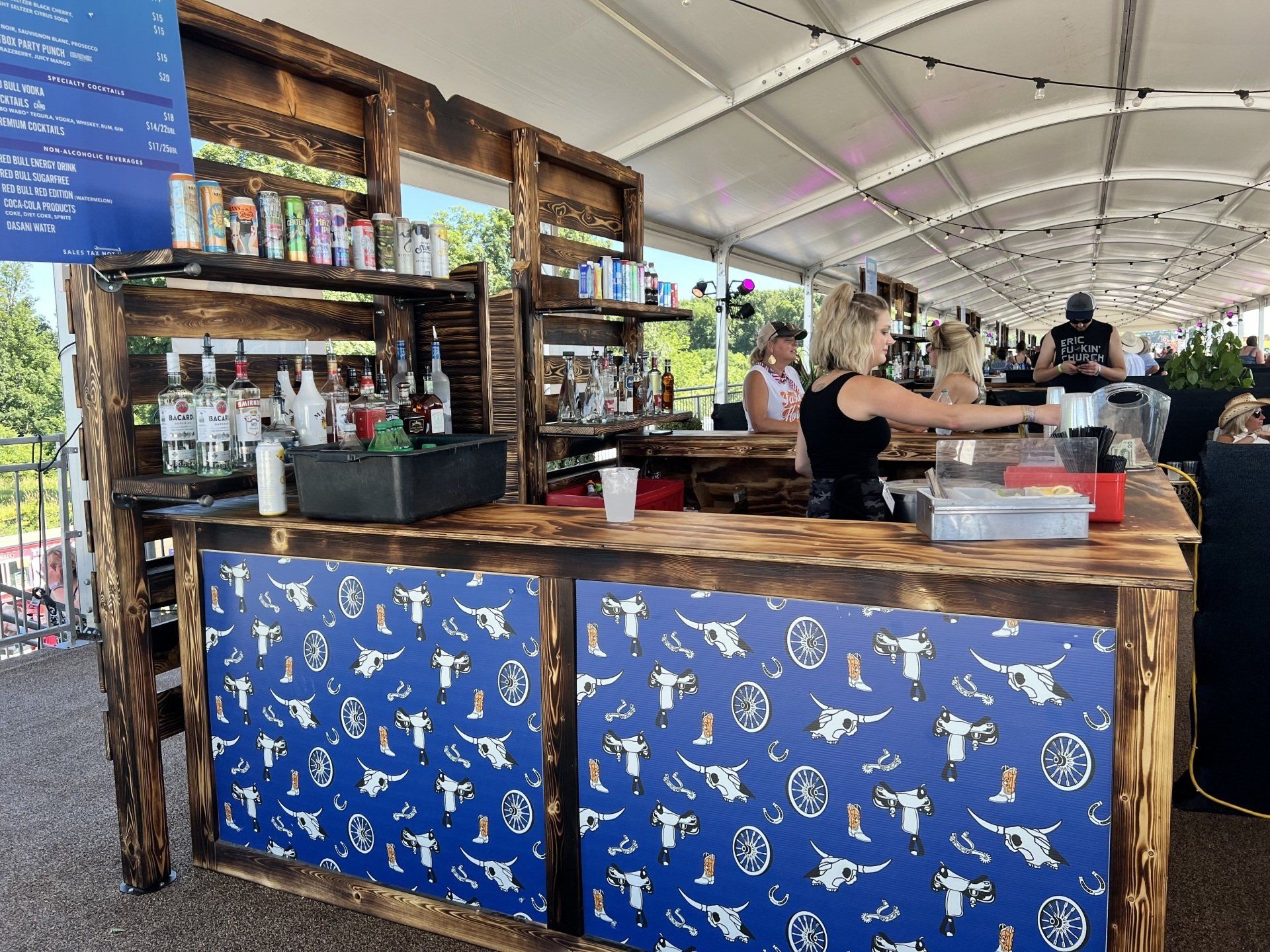 A woman is standing behind a wooden bar in a tent.