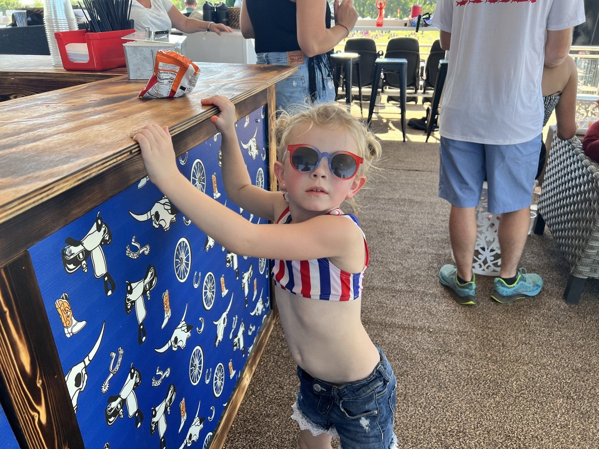 A little girl in a bikini and sunglasses is leaning on a counter.