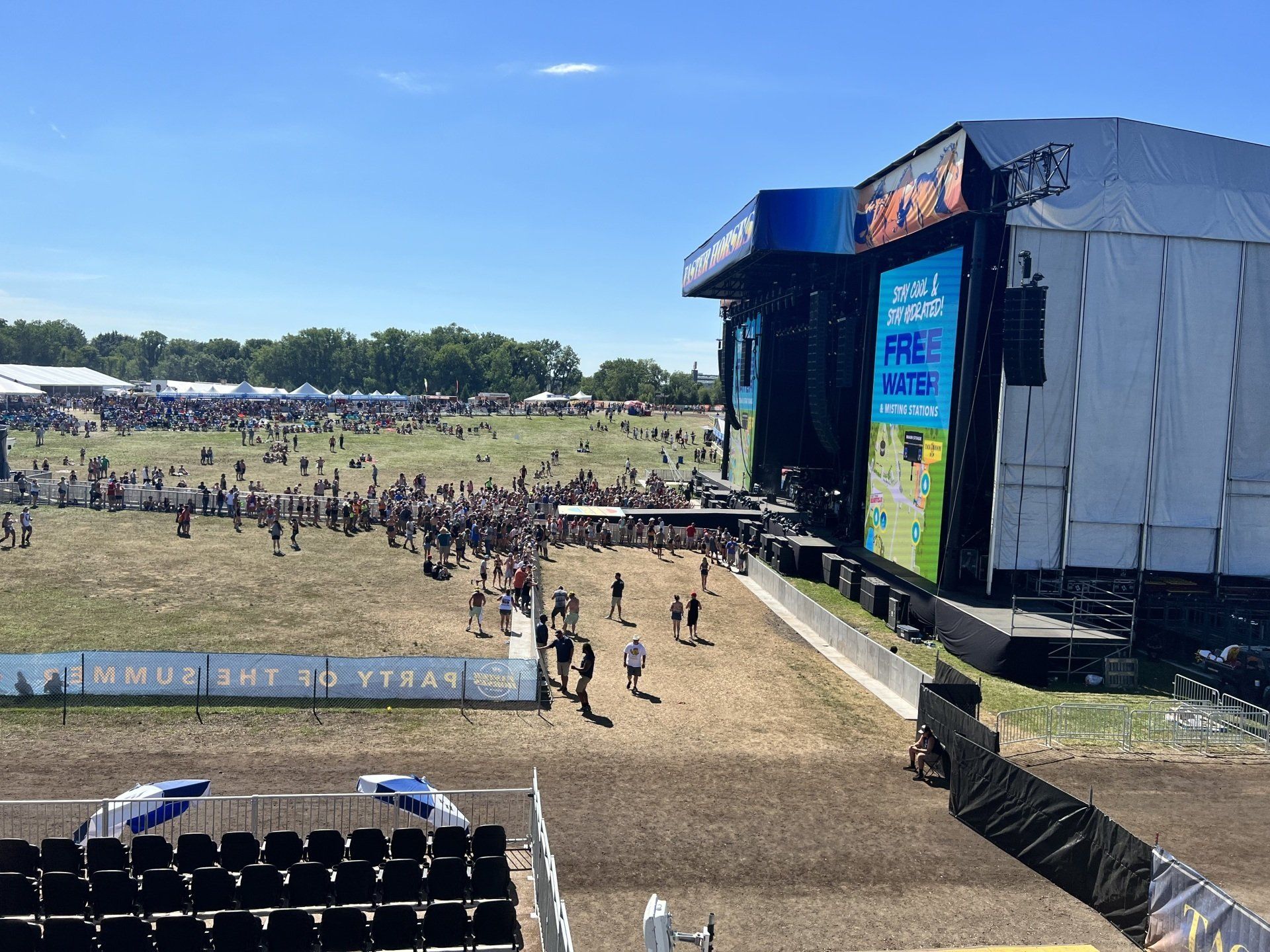 A large stage at a music festival with people walking around it.
