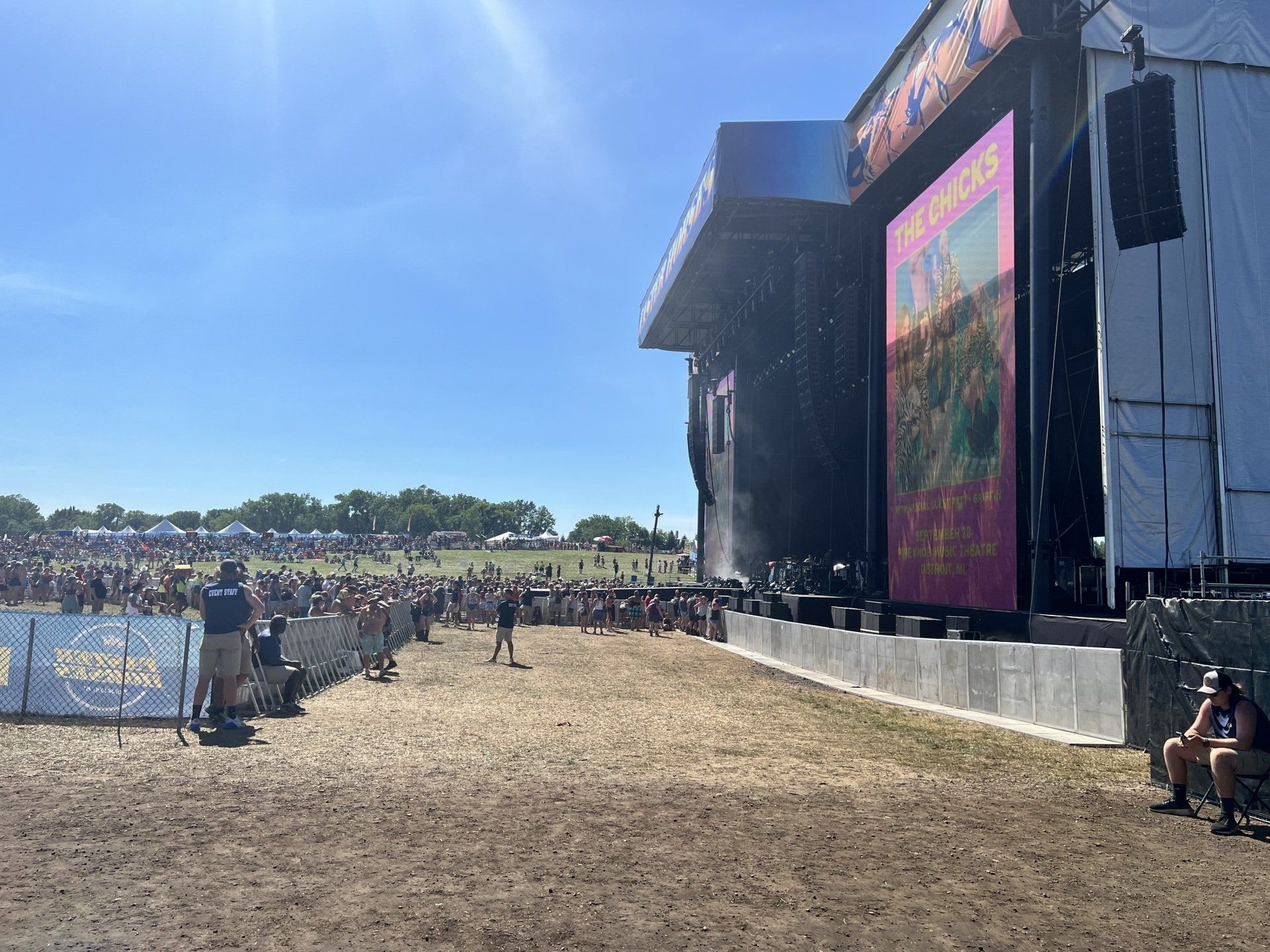 A large screen is hanging from the side of a stage at a music festival.