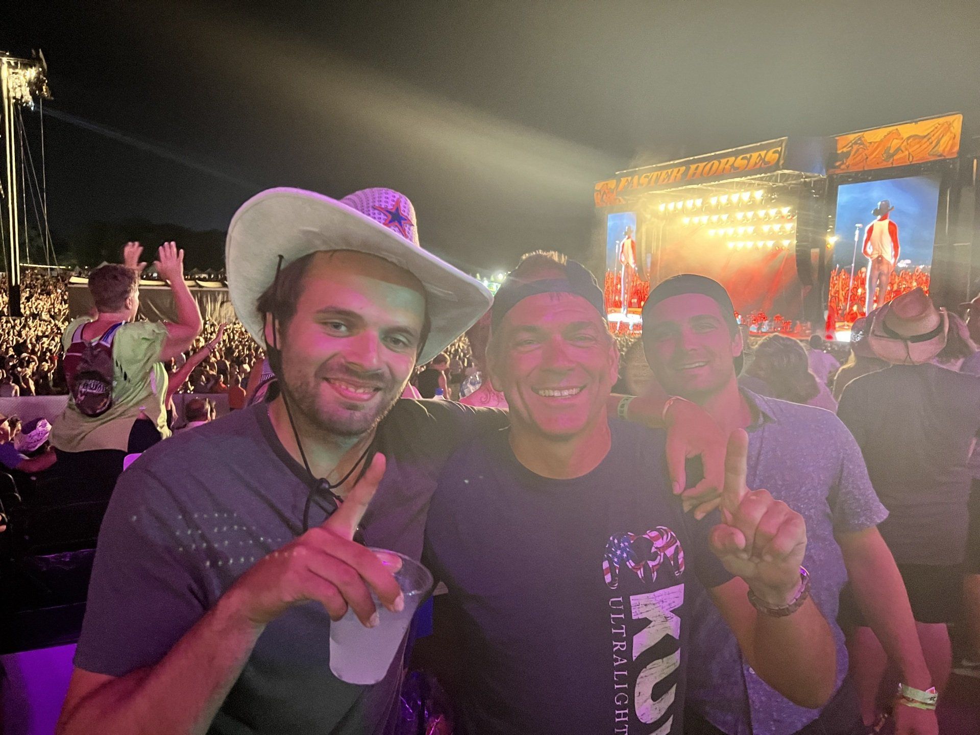 Three men are posing for a picture at a concert . one of the men is wearing a cowboy hat.