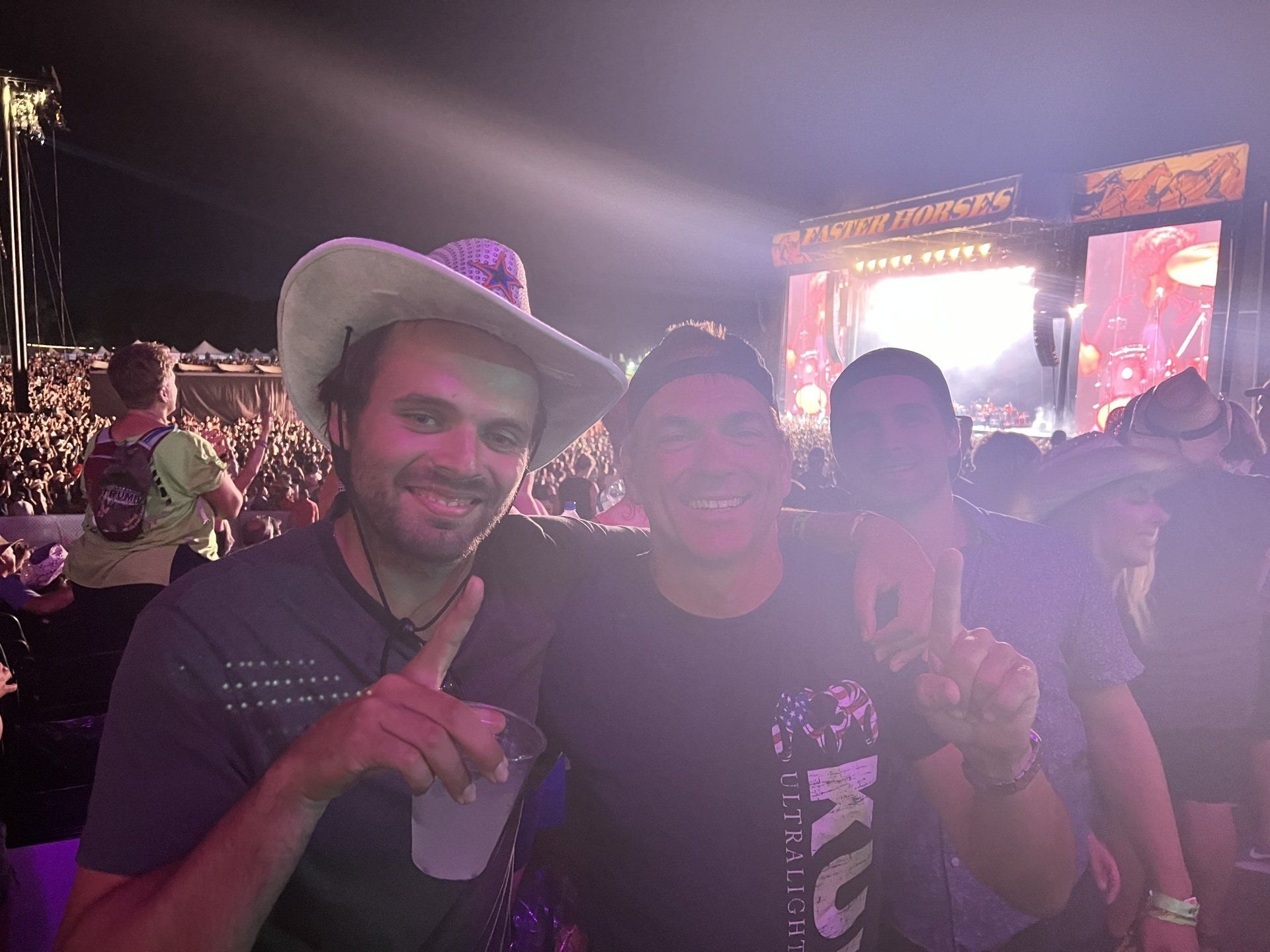 Two men in cowboy hats are posing for a picture at a concert.