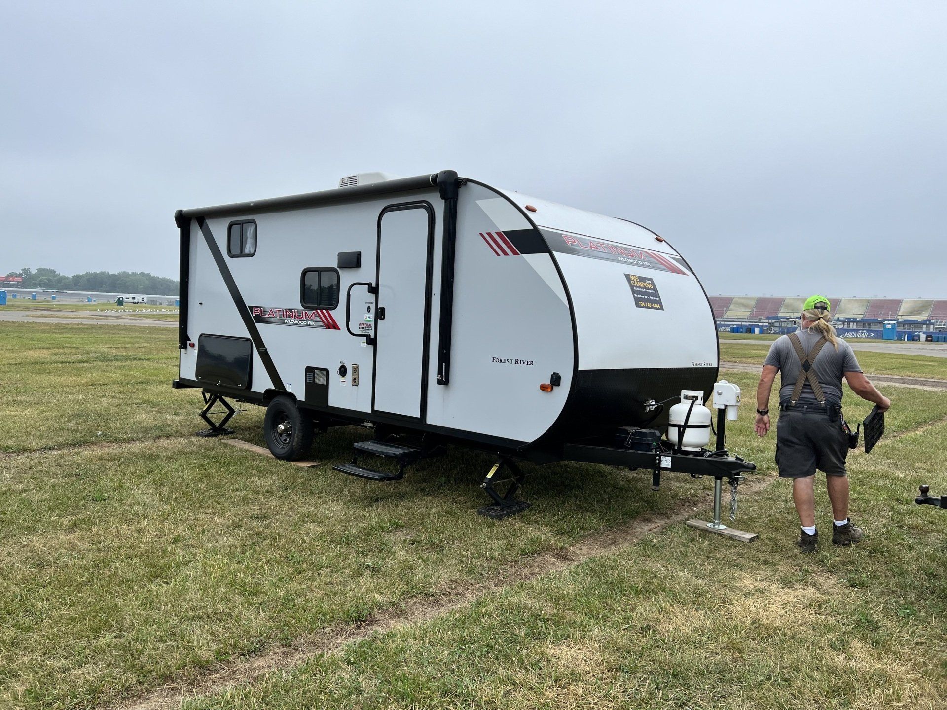 A man is standing next to a small trailer in a grassy field.