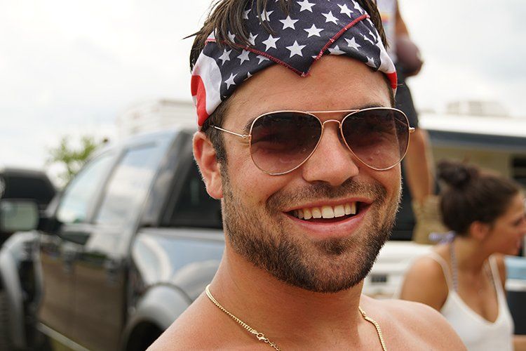 A man wearing sunglasses and an american flag headband smiles for the camera