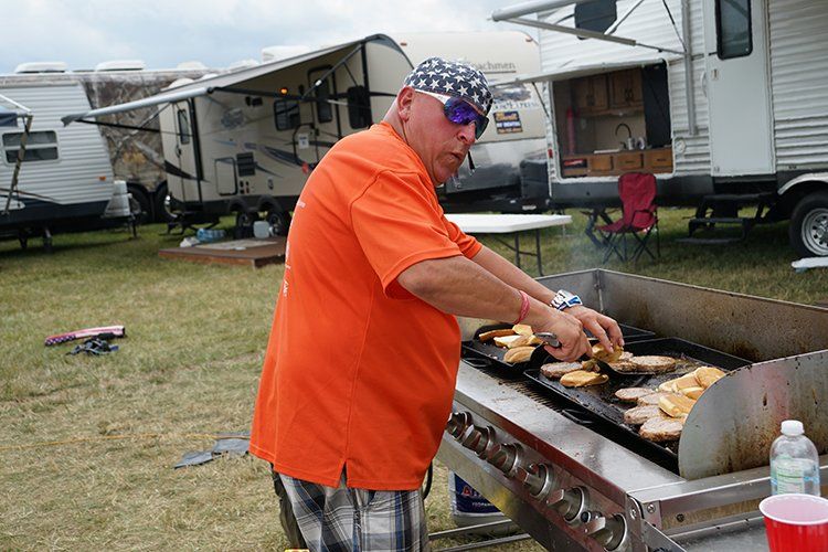 A man in an orange shirt is cooking food on a grill.