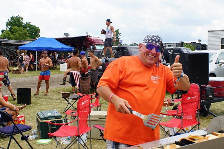 A man in an orange shirt is holding a spatula and giving a thumbs up.