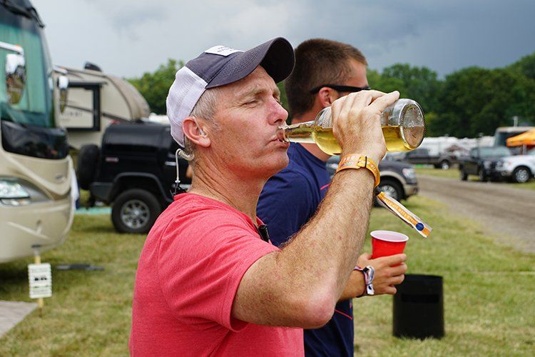 A man is drinking beer from a bottle while another man holds a red cup.