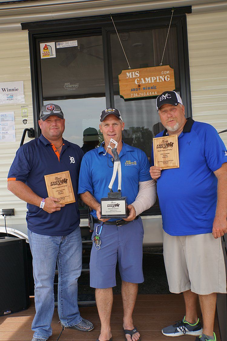 Three men are standing next to each other holding trophies.