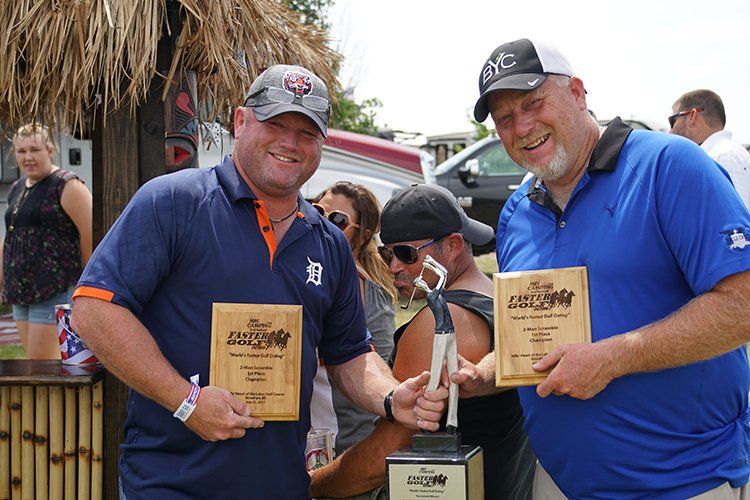 Two men are standing next to each other holding trophies.
