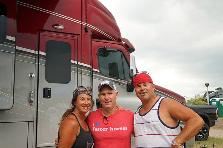Three people are posing for a picture in front of a horse trailer.