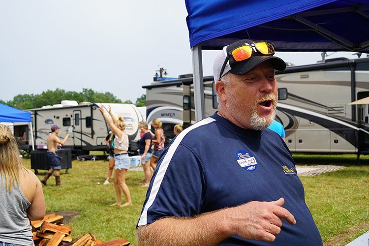 A man wearing sunglasses and a hat is standing under a tent in a field.