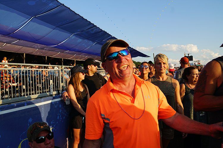 A man wearing sunglasses and an orange shirt is standing in a crowd of people.