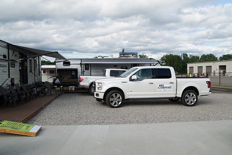 A white truck is parked in a gravel lot next to a trailer.