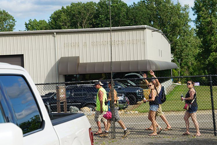 A group of people are walking across a chain link fence in front of a building.