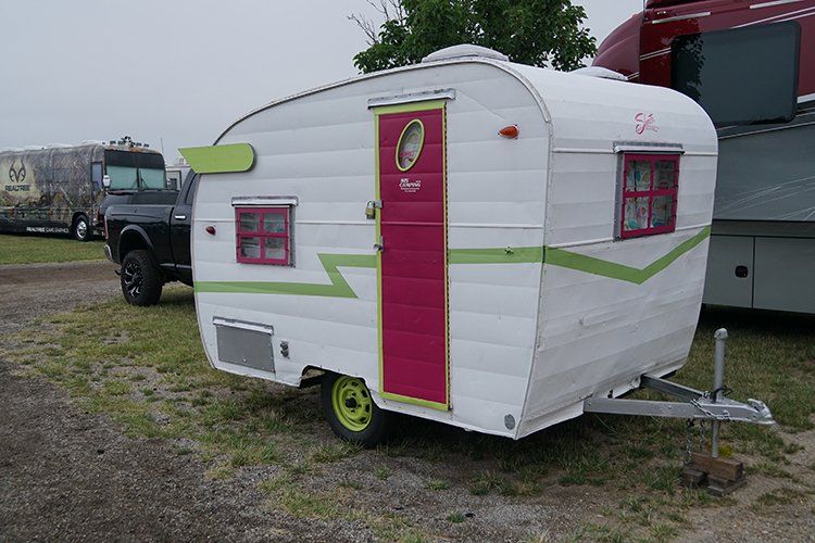 A small white trailer with a pink door is parked in a grassy field.
