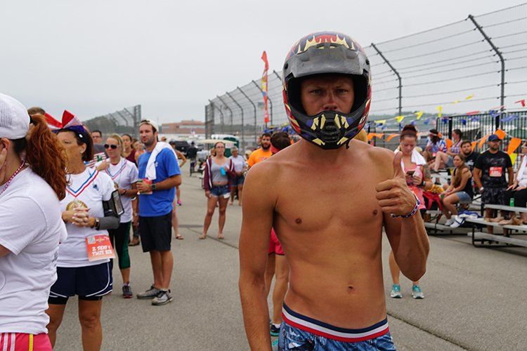 A shirtless man wearing a helmet is standing in front of a crowd of people.