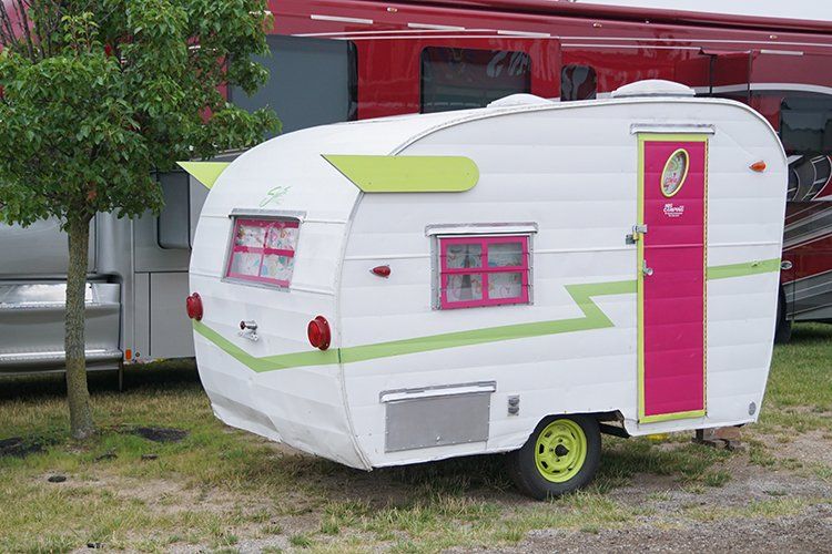 A white trailer with a pink door is parked next to a red rv.