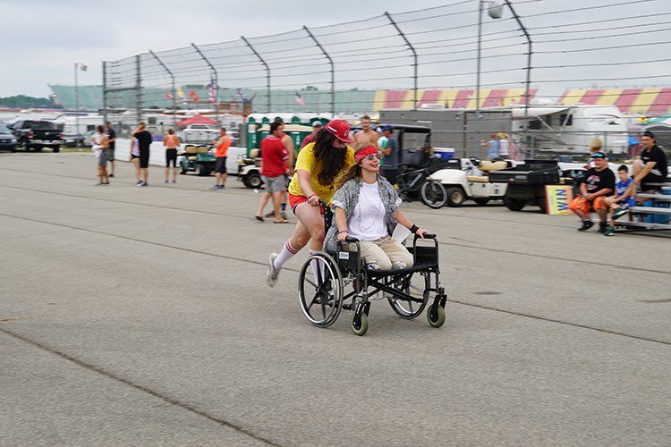 A woman pushes another woman in a wheelchair on a race track