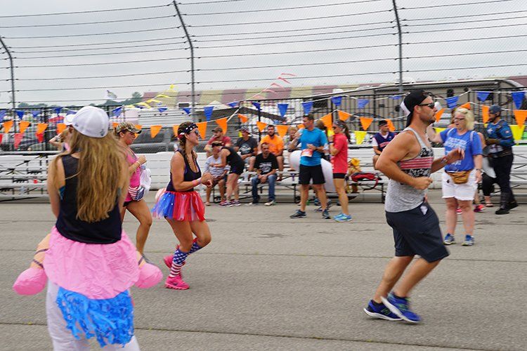 A group of people are dancing in a parking lot at a race track.