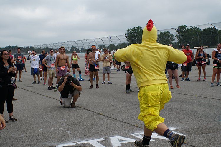 A man in a chicken costume is running in front of a crowd