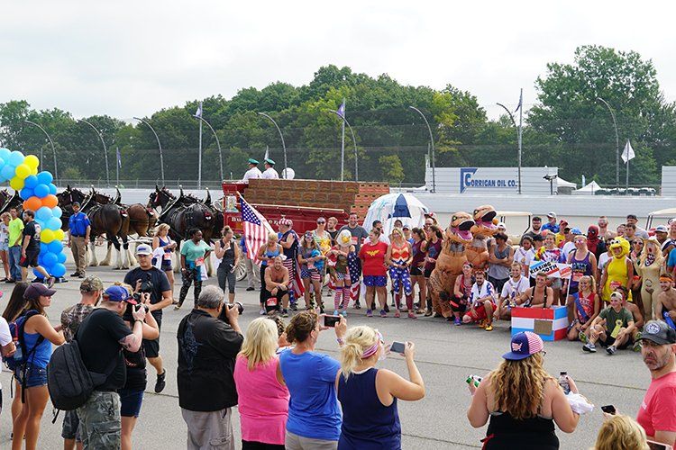 A crowd of people are watching a parade with horses pulling a wagon.