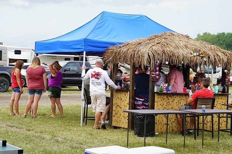 A group of people are standing around a tiki bar in a field.