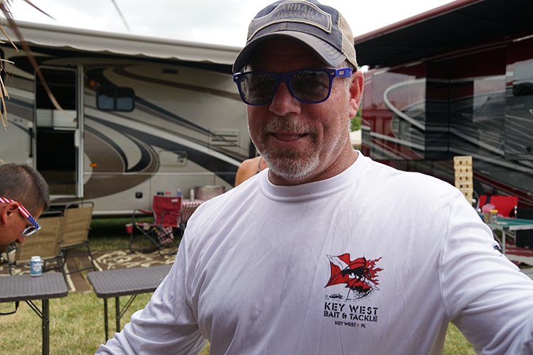 A man wearing sunglasses and a hat is standing in front of a trailer.