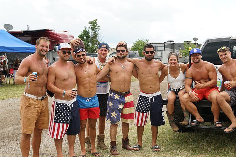 A group of shirtless men are posing for a picture while sitting on the back of a truck.