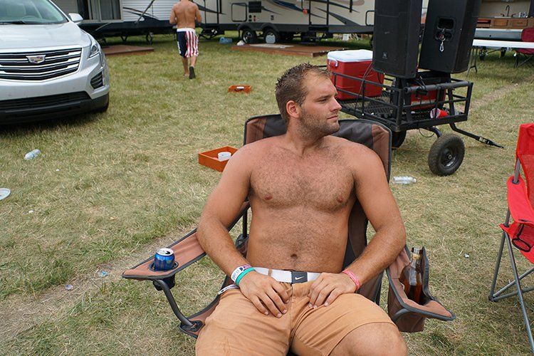 A shirtless man is sitting in a chair in a field.