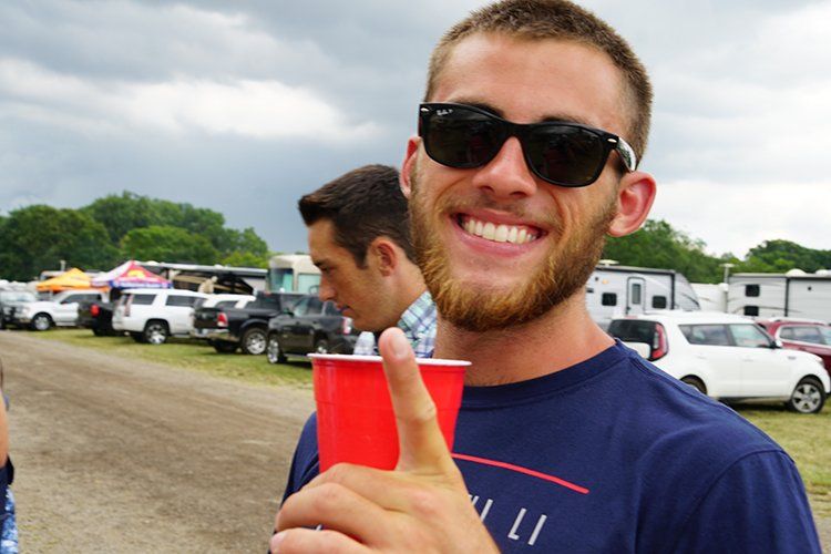 A man wearing sunglasses is holding a red cup and giving a thumbs up.
