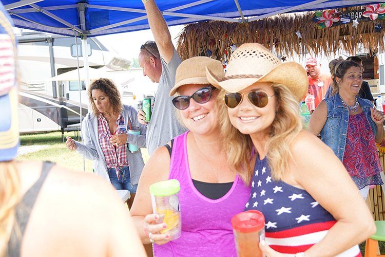 Two women are standing next to each other under a blue tent holding drinks.