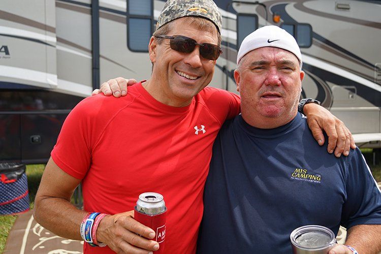 Two men are posing for a picture and one is holding a can of soda