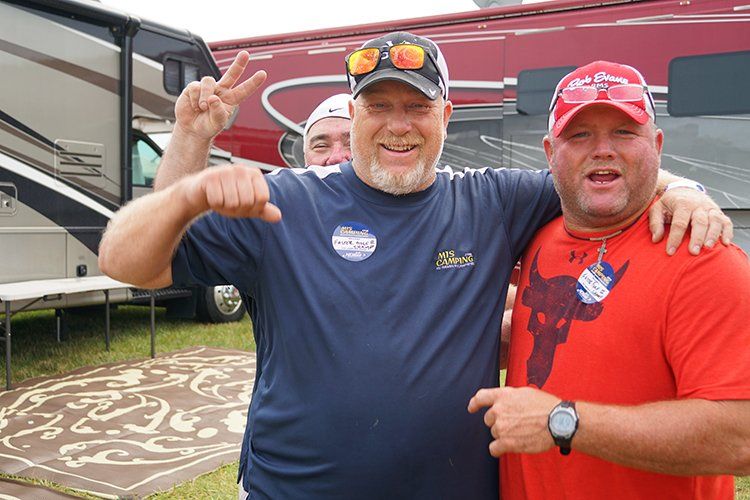 Three men are posing for a picture in front of a rv.