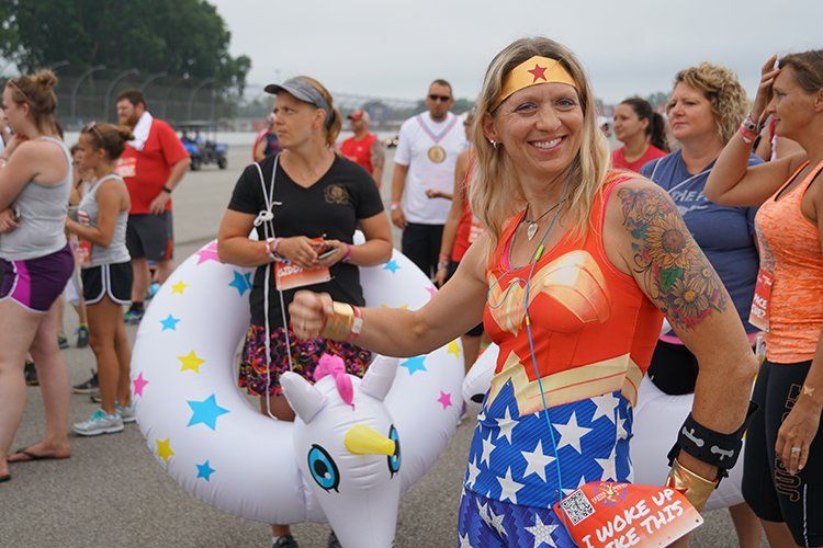 A woman in a wonder woman costume is holding an inflatable unicorn float.