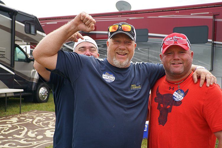 Three men are posing for a picture in front of a rv.