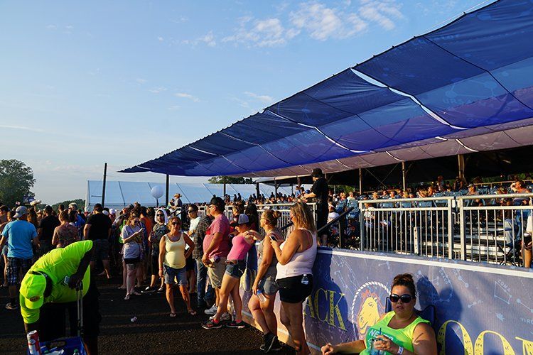 A crowd of people are standing under a blue canopy at a concert.