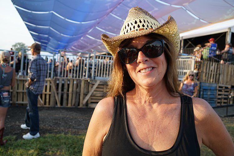 A woman wearing a cowboy hat and sunglasses is smiling for the camera.