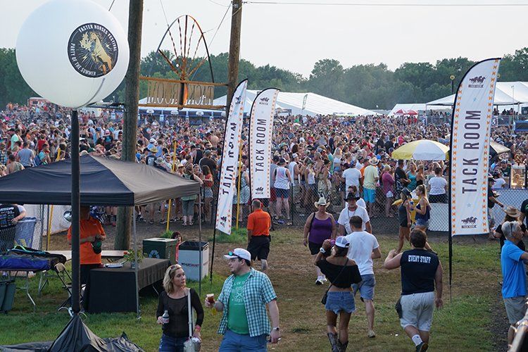 A crowd of people walking in a field with a sign that says tack room