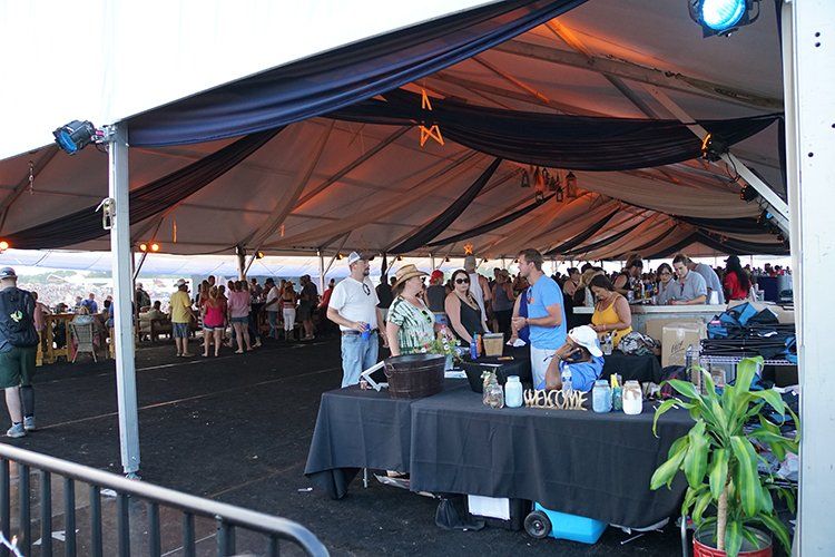 A group of people are standing around tables under a tent.