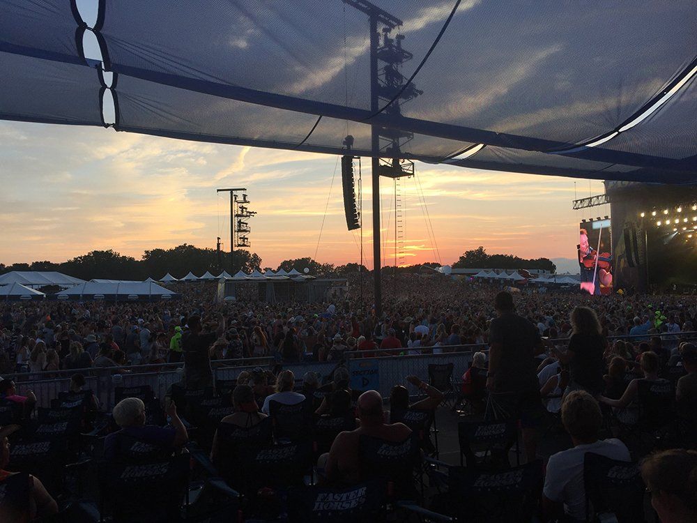 A crowd of people are watching a concert at sunset.