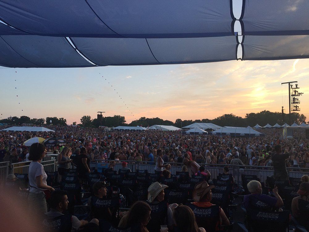 A crowd of people are gathered under a blue canopy at a concert