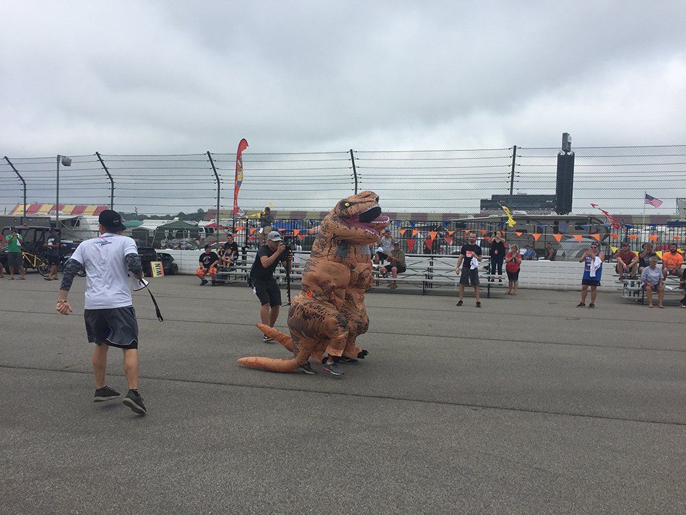 A group of people are standing around a t-rex costume.