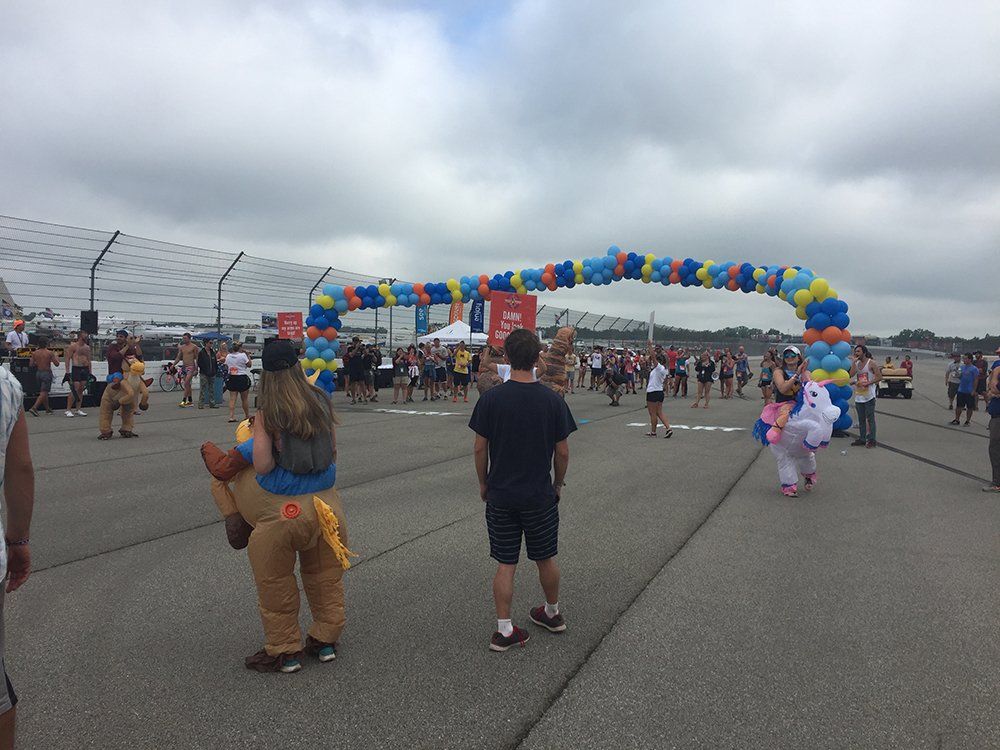 A group of people are standing in a parking lot with balloons in the background.
