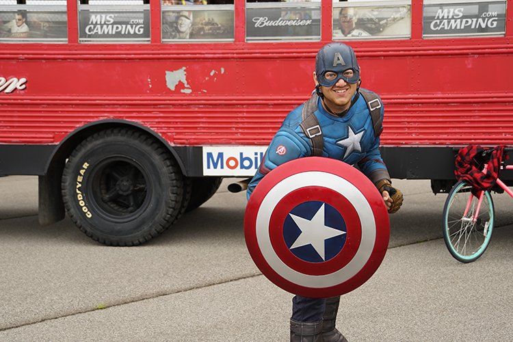 A man dressed as captain america is holding a shield in front of a red bus.