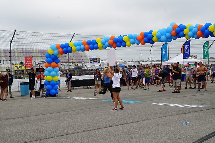 A woman is standing in front of a balloon arch at a race track.