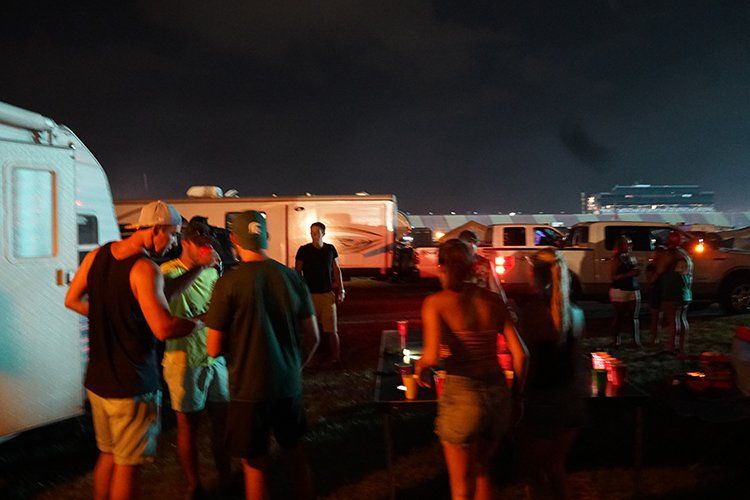 A group of people are standing in a parking lot at night.