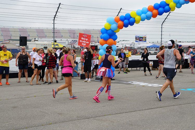 A group of people are running in a race with balloons in the background.